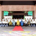 Group of Formally Dressed Officials in White Uniforms Posing for a Ceremony on a Red Carpet in Front of a Government Building, with Central Dignitaries in Bright Traditional Attire Beneath a Signboard.**oops**