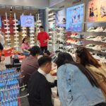 Busy Footwear Store with Wall Displays of Sneakers; Customers Try on Shoes While Staff Assist.