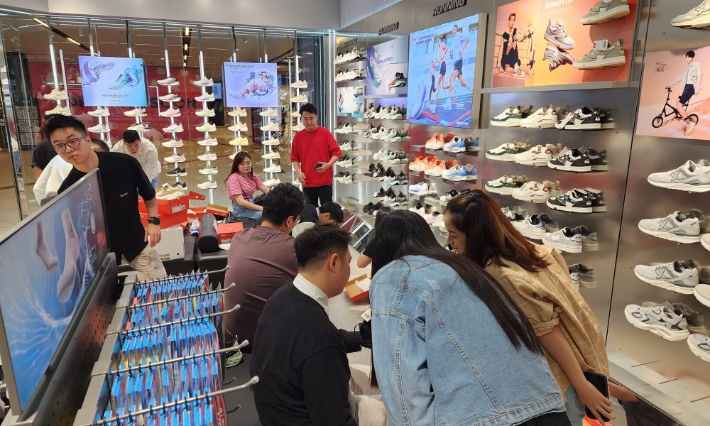 Busy Footwear Store with Wall Displays of Sneakers; Customers Try on Shoes While Staff Assist.