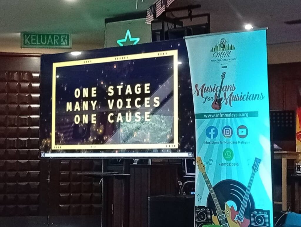Mfm Pc - Nmh | Nmh Screen Displaying “one Stage, Many Voices, One Cause” Beside a Musicians for Musicians Malaysia Banner.